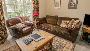 A living room with a leather armchair, a brown sofa, a wooden coffee table, and a television on a wooden stand. - Rowan Cottage (Ambleside)