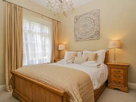 A bedroom with a wooden bed, beige curtains, a chandelier, and a decorative wall piece.