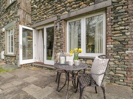 A stone building with a patio area featuring a round table and two chairs, a vase with yellow flowers, and a lantern.