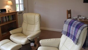 Une pièce comprenant un fauteuil en cuir beige, un pouf assorti et une bibliothèque en bois.