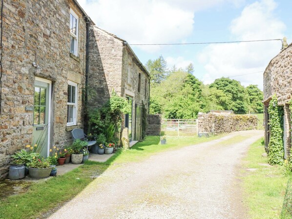 Un étroit sentier de gravier mène à un bâtiment en pierre dont la porte est marquée de l’inscription « The Cottage ».