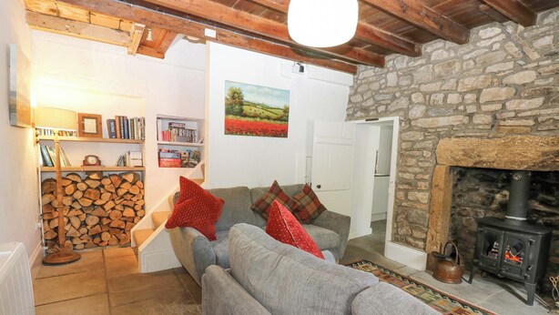 Un salon chaleureux avec une cheminée en pierre, un canapé gris et une bibliothèque remplie de livres et d’objets décoratifs.