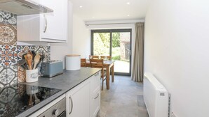 Une cuisine moderne avec des armoires blanches, un comptoir noir et un dosseret carrelé. On y trouve un coin repas avec une table et des chaises, et une vue sur l’extérieur grâce à une porte vitrée.