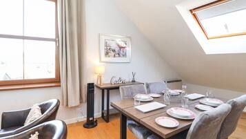 A dining area with a table set for four, a standing fan, and a window with curtains.