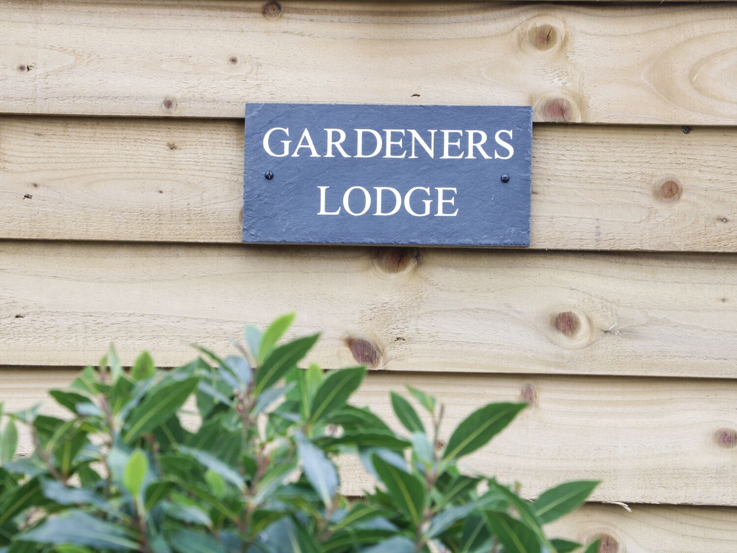 A sign reading "GARDENERS LODGE" mounted on a wooden wall.
