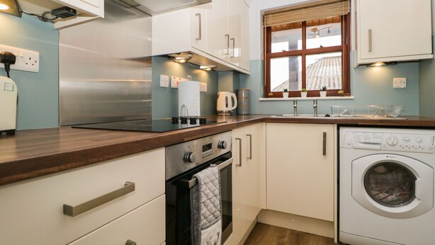 A compact kitchen with a built-in oven, a washing machine, and a window with blinds. - Andra Ghyll (Keswick)