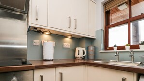 A modern kitchen with stainless steel appliances, white cabinets, and a window with plants. - Andra Ghyll (Keswick)