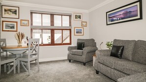 A living room with a dining table, two grey armchairs, a grey sofa, and a large window with blinds. - Andra Ghyll (Keswick)