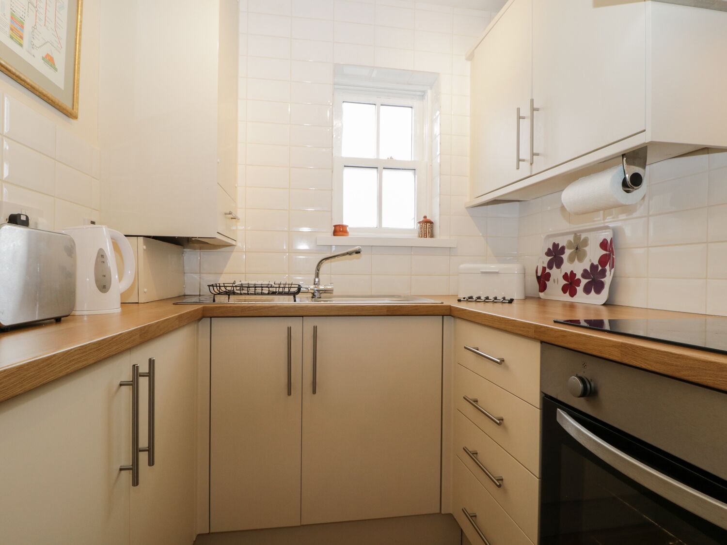A kitchen with white cabinets, a wooden countertop, a sink, a toaster, and a window above the sink.
