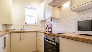 Een moderne keuken met witte kastjes, een houten aanrechtblad, een inbouwoven en een magnetron.