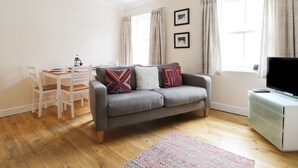 Een moderne woonkamer met een grijze bank, witte stoelen, een eettafel en een televisie op een dressoir.