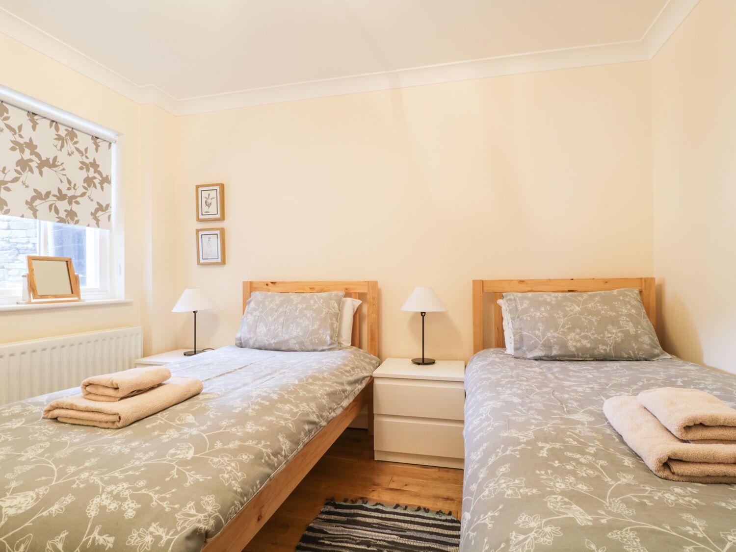 A bedroom with two single beds, each with a wooden headboard, a nightstand, a lamp, and a window with a view.