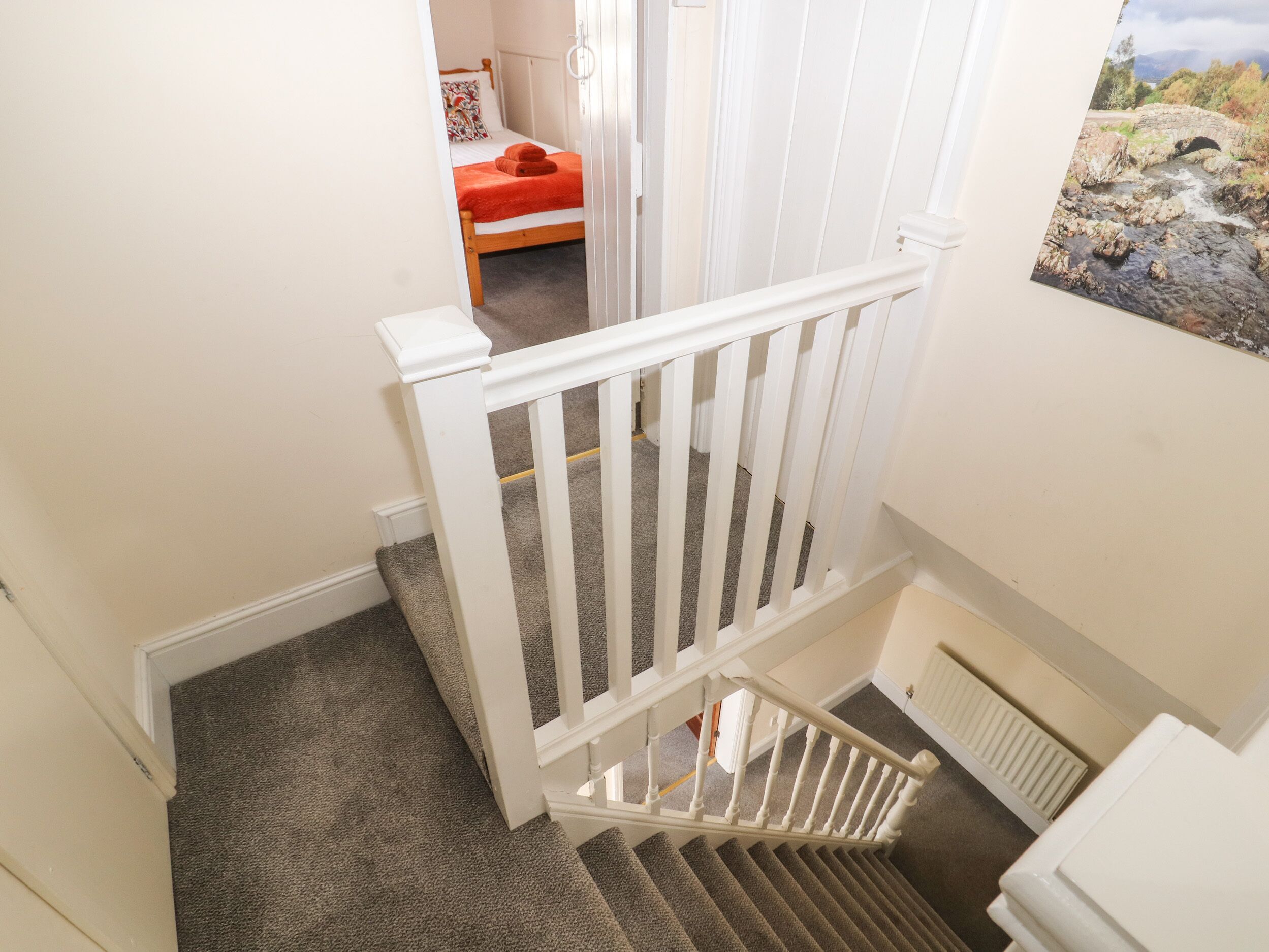 A staircase with white railings leading to a bedroom with a bed and a painting of a bridge.