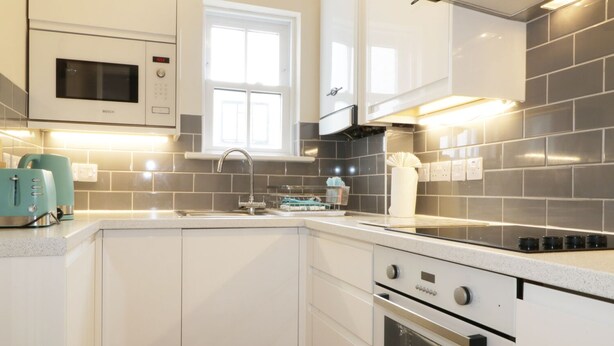 Una cocina moderna con armarios blancos, un microondas Bosch, una campana extractora de acero inoxidable y un horno empotrado.