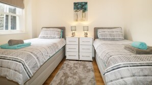 Un dormitorio con dos camas individuales, una ventana con persianas, un cuadro en la pared y dos mesitas de noche con lámparas.