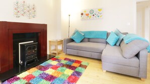 Una sala de estar con chimenea, un sofá gris con cojines azules, un tapete colorido y decoración en la pared.