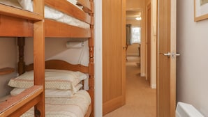 A room with bunk beds, a wooden door, and a hallway leading to another room. - Treetops (Windermere)