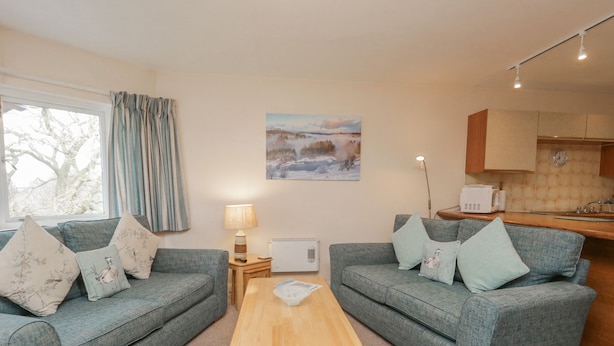 A cozy living room with two grey sofas, a wooden coffee table, and a painting of a snowy landscape. - Treetops (Windermere)