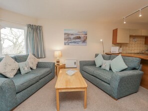 A cozy living room with two grey sofas, a wooden coffee table, and a painting of a snowy landscape.