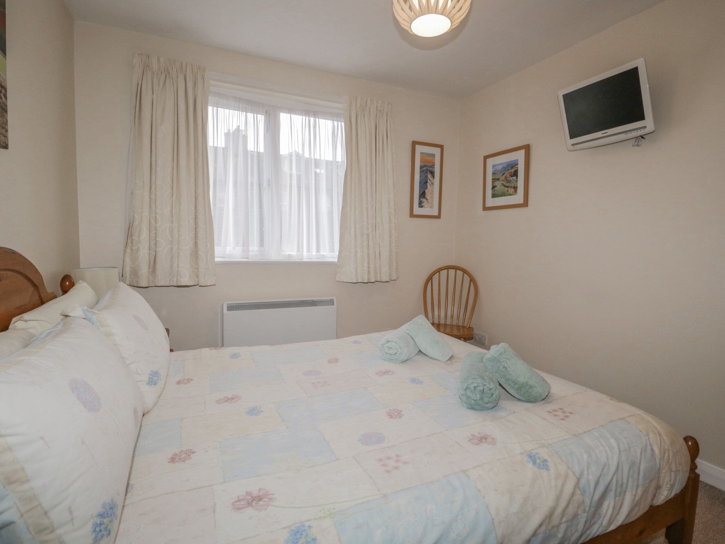 A bedroom with a bed, a chair, a TV, and a window with curtains.