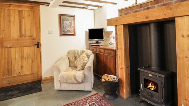 A cozy living room with a fireplace, a television, and a comfortable armchair. - The Old Barn (Seascale)