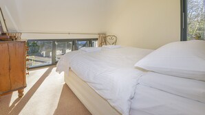 A bedroom with a large bed, a wooden dresser, and a view of the outdoors through a window. - The Bakehouse (Newton Abbot)
