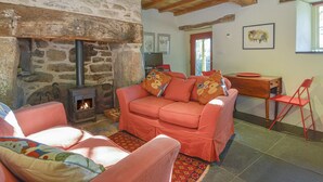 A cozy living room with a stone fireplace, wooden beams, a sofa with colorful cushions, and a dining area with a red chair. - The Bakehouse (Newton Abbot)