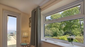 Una habitación con vistas a la vegetación a través de una ventana, una mesita con una lámpara y un radiador.