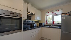 Una cocina moderna con armarios blancos, horno empotrado, microondas y refrigerador.