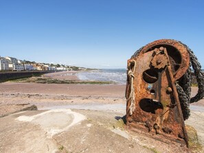 A coastal scene with a rusted metal structure, a sandy beach, and buildings in the background. - Exe View (Dawlish)