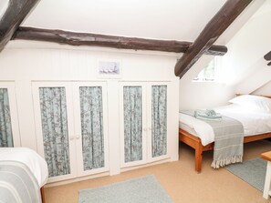 A bedroom with a sloped ceiling, a wooden bed, a wardrobe with floral curtains, and a small window. - Castle View (Minehead)