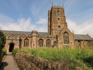 A historic stone building with a tall tower, arched windows, and a pathway leading to the entrance. - Castle View (Minehead)