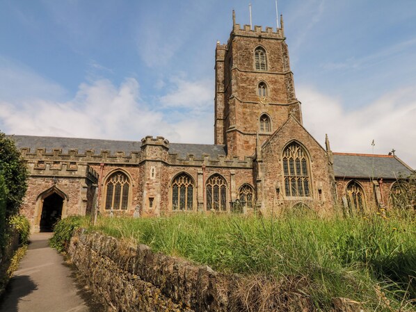 A historic stone building with a tall tower, arched windows, and a pathway leading to the entrance. - Castle View (Minehead)