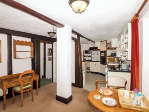 A dining area with a wooden table and chairs, a kitchen in the background, and a red curtain on the right. - Castle View (Minehead)