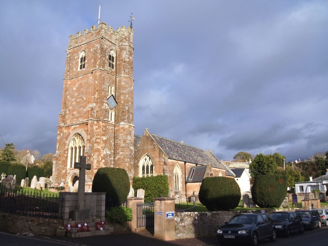 A historic church with a prominent tower, a cemetery, and a parking area with cars.