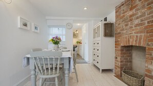 A dining area with a white table and chairs, a brick fireplace, and a kitchen in the background. - 1 The Quay (Exmouth)