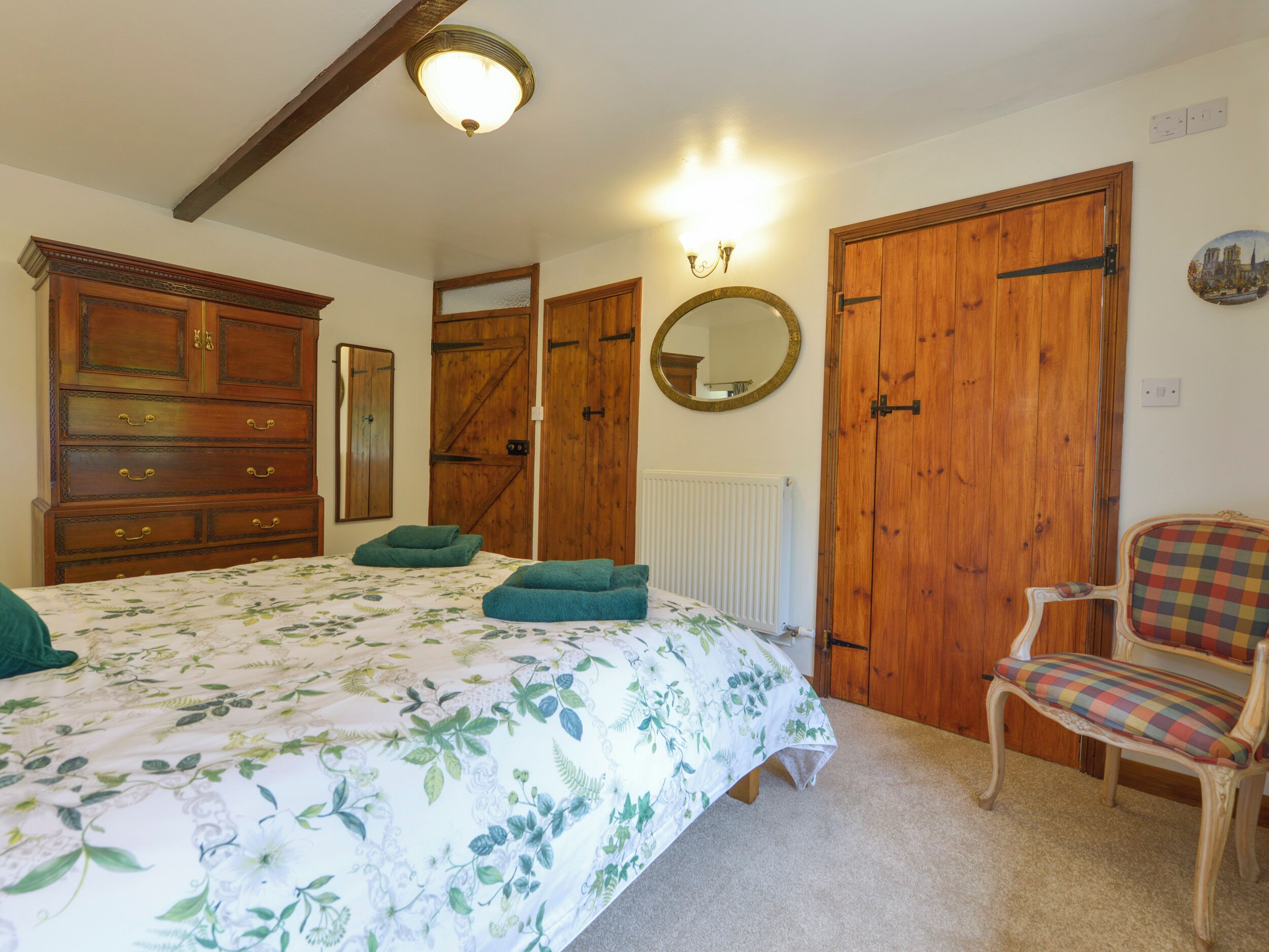 Un dormitorio con una cama grande, un armario de madera, una silla y un espejo en la pared.