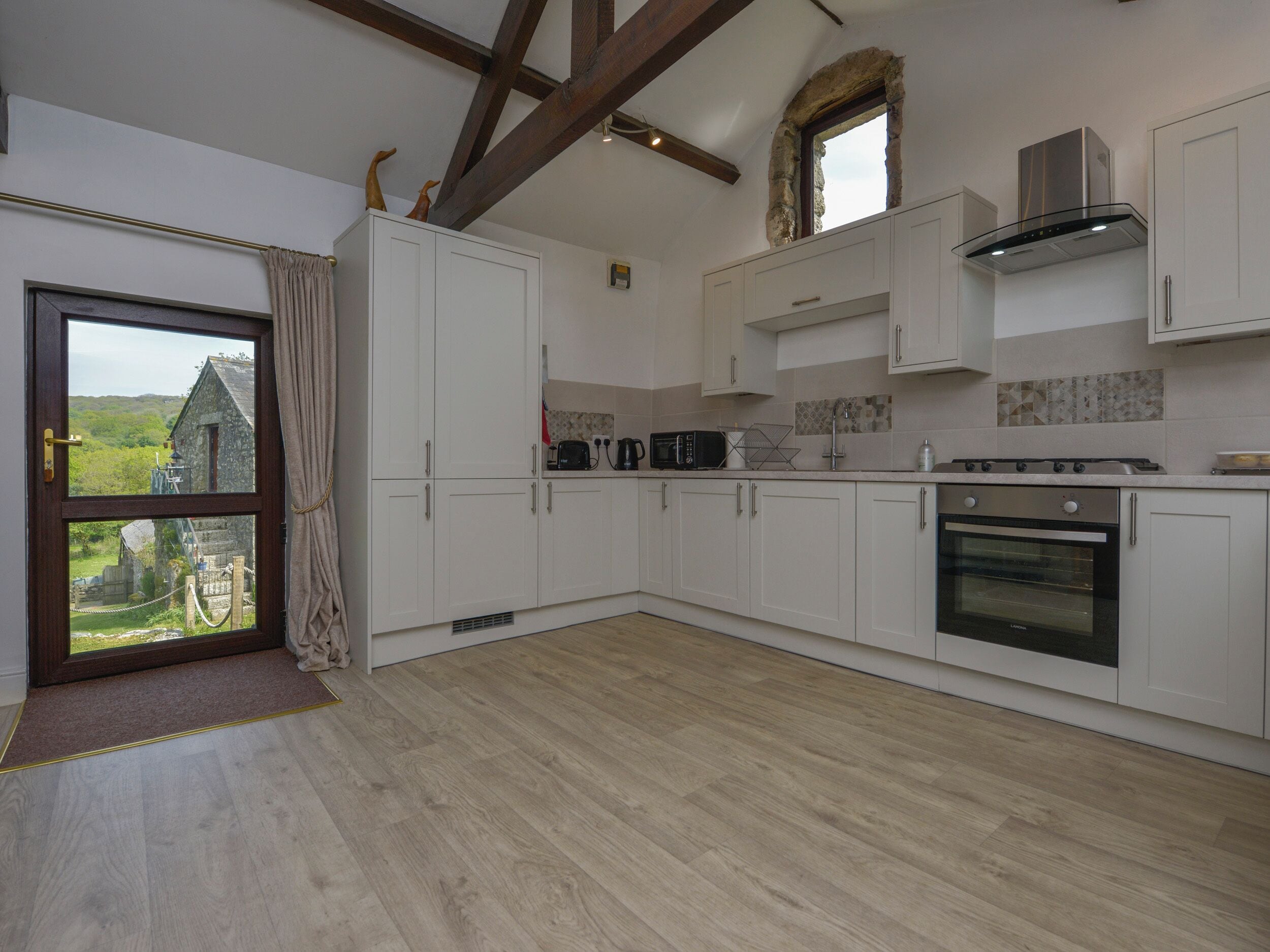 Una cocina moderna con armarios blancos, horno empotrado y ventana en arco de piedra.