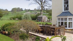Un patio con mesa y sillas, rodeado de un jardín con un árbol grande y una estructura de piedra.