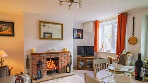 A cozy living room with a fireplace, a television, and a dining area with a table set for two. - Poppy Cottage (Blandford Forum)