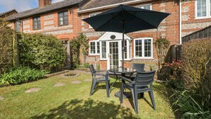 A brick house with a garden patio featuring a table and chairs, surrounded by greenery and a wooden fence. - Poppy Cottage (Blandford Forum)