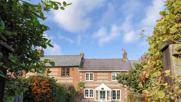 A traditional brick house with a well-maintained garden, a small white door, and a clear sky. - Poppy Cottage (Blandford Forum)