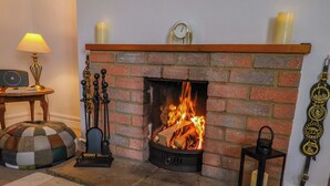 A fireplace with a brick surround, a mantel with a clock, and a candle holder to the right. - Poppy Cottage (Blandford Forum)