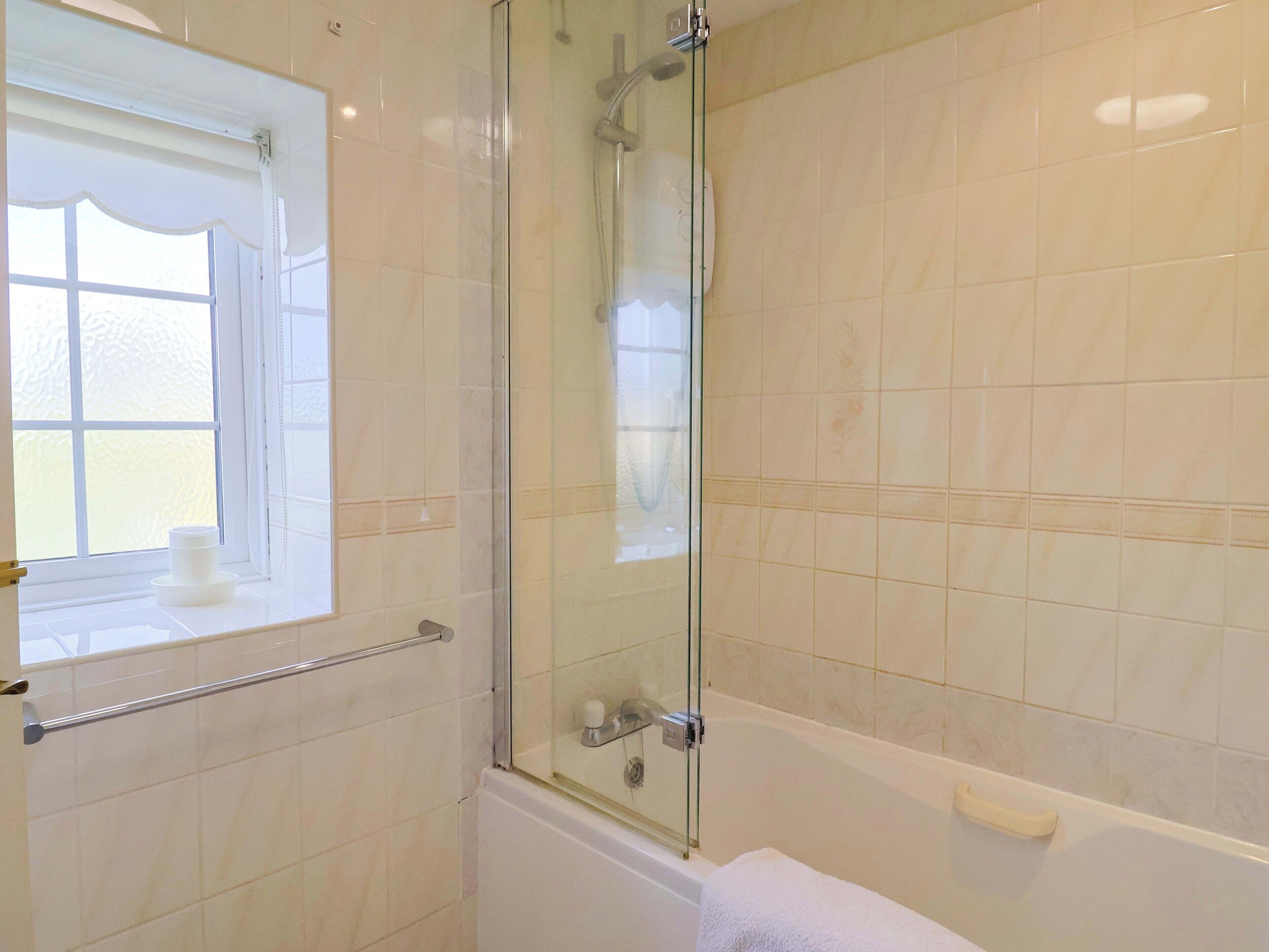 Un baño con ducha envuelta en vidrio, una bañera y una ventana con un perchero para toallas.