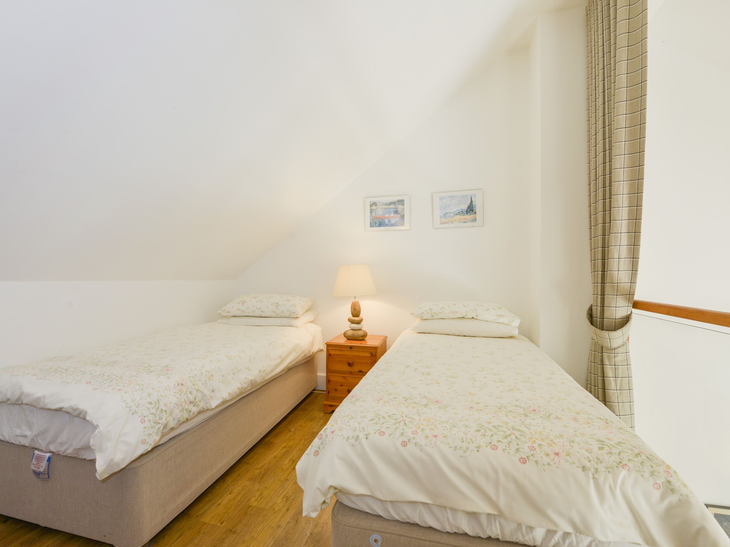 A twin room with two single beds, a nightstand with a lamp, and two framed pictures on the wall.