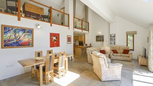 Amplia sala de estar con mesa de comedor, sillas, sofá y un alto techo con tragaluces.