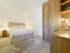Une chambre à coucher comprenant un lit, des tables de chevet, une armoire en bois et une petite table avec une lampe.