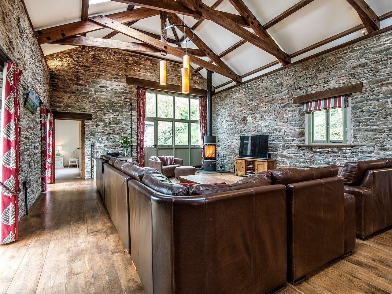 A rustic interior with a stone wall, wooden beams, a leather sofa, a fireplace, and a television.