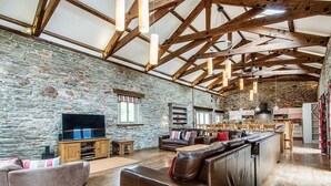 A spacious living area with a stone wall, wooden beams, leather sofas, and a flat-screen TV. - Mill Barn (Kingsbridge)
