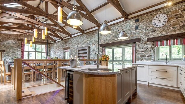 A spacious kitchen with a central island, wooden beams, stone walls, and pendant lighting. - Mill Barn (Kingsbridge)